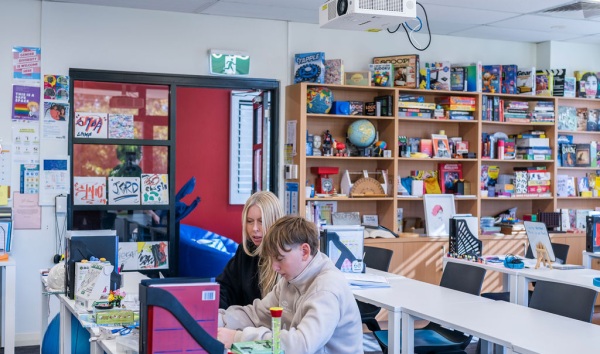 A woman helping a boy do schoolwork in a classroom at the Youth Futures Community School Midland