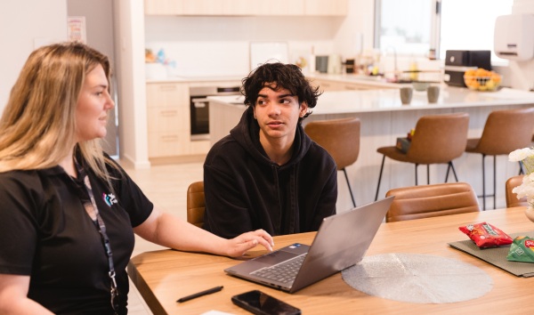 Teenager talking to woman using laptop at kitchen table of youth futures acommodation