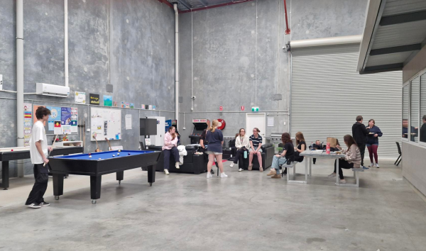 Young people relax and socialise in a large indoor common space at Youth Futures' Anchor Point Bayswater, with a pool table, seating areas, and tables in view.